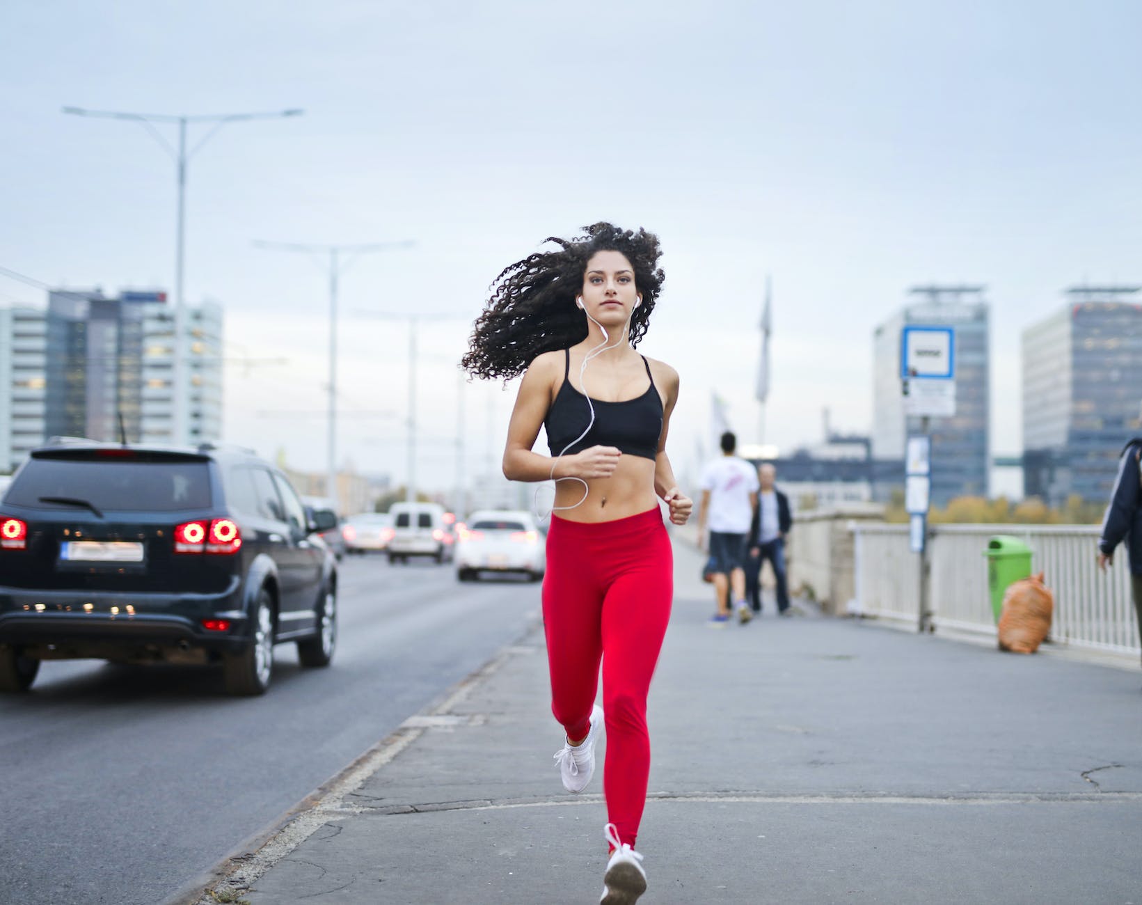 photo of woman listening to music on earphones running down a sidewalk