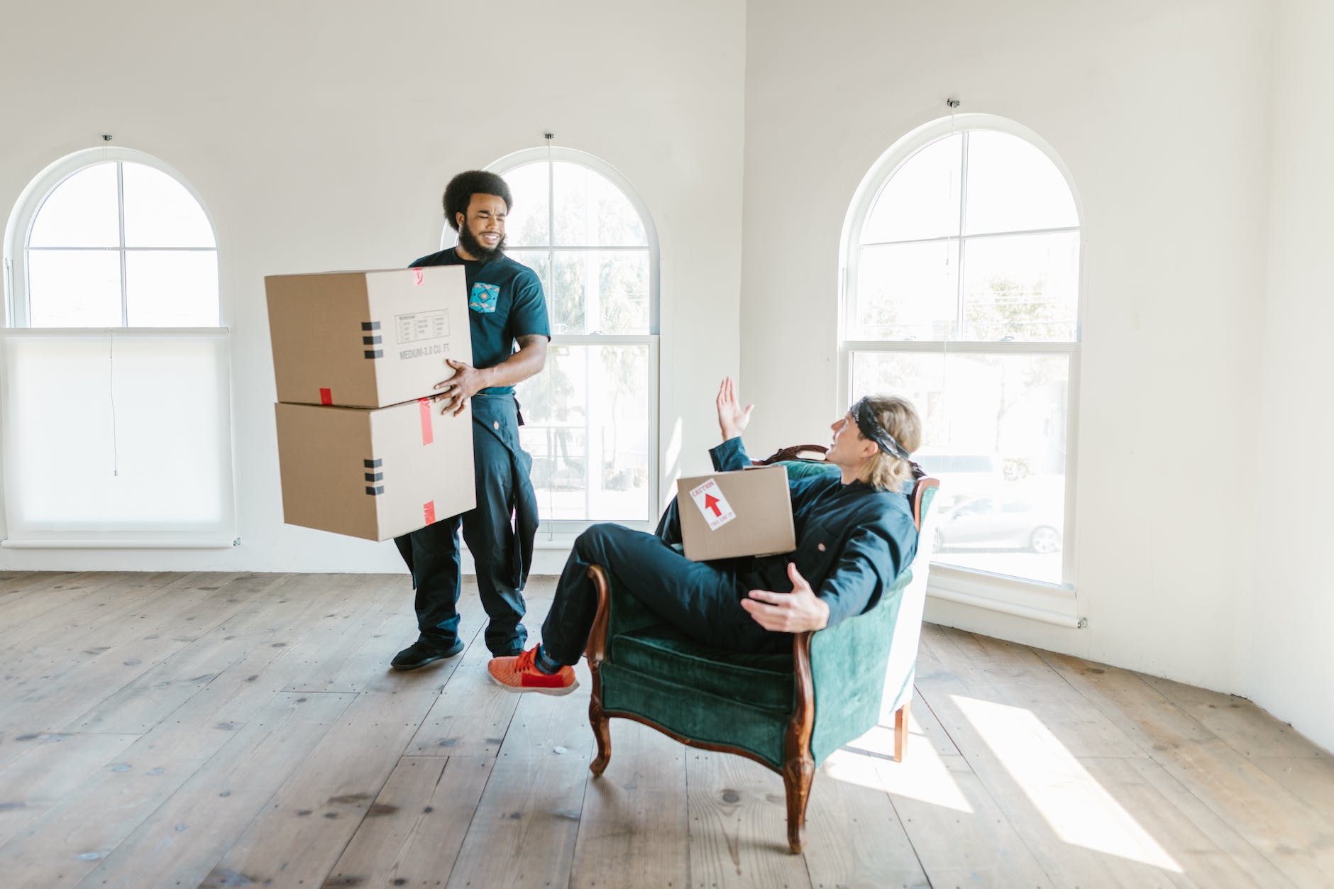 a man standing carrying boxes talking to a man sitting on a chair