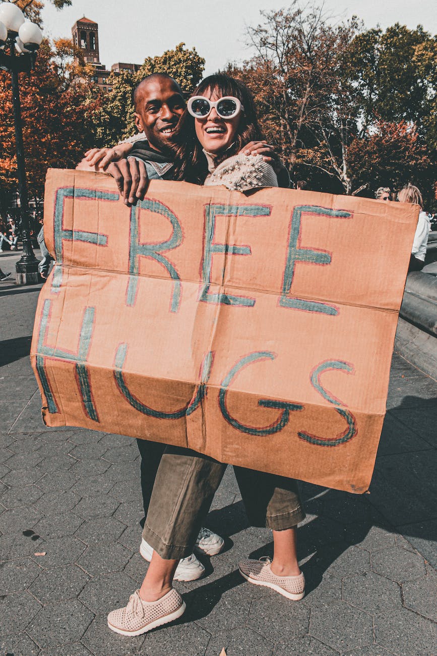 man and woman holding free hugs signage